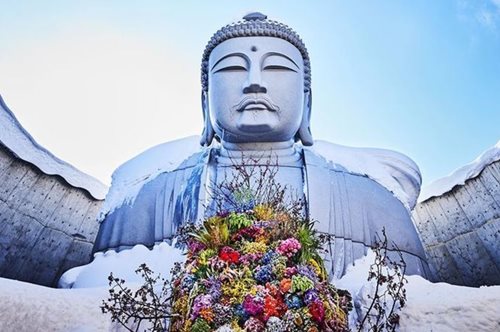 Ο Βούδας κρατά μια αγκαλιά λουλούδια, ευχή για παγκόσμια ειρήνη