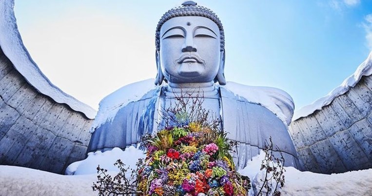 Ο Βούδας κρατά μια αγκαλιά λουλούδια, ευχή για παγκόσμια ειρήνη